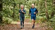 © Jiraporn - Elderly couple jogging together along a scenic forest path, enjoying active and healthy outdoor lifestyle.