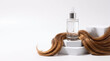 © astri - Luxury hair serum bottle on podium with lock of wavy brown hair