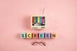 © Fahad - A retro television with colorful screen display sits atop colorful alphabet blocks spelling out 'SCREEN' with eyeglasses below on a pink background, symbolizing vintage media and entertainment