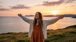 © MdJilu - A happy young woman standing on a grassy hill with arms outstretched enjoying the beautiful golden sunset over the calm ocean water