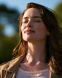 © Kowit - Young woman with closed eyes enjoying sunlight outdoors, expressing calm and relaxation with natural background.