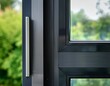 © Leanne - close up detail of a modern triple glazed window with a slim dark aluminium frame and airtight seals against a softly blurred green garden for energy efficient passive house construction