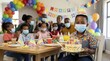 © Xenia - African American boy wearing a face mask holding a birthday cake with lit candles. Family celebrating safely with masks in a decorated room. Pandemic birthday party concept