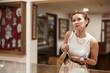 © JackF - Deep in thought interested middle aged woman, wearing white sleeveless top and gold accessories, attentively examining displayed artifacts in museum