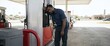 © Xenia - Exhausted Black gas station attendant leaning against pump. Tired male worker resting in hot sun. Summer heatwave and physical labor concept