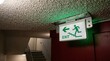 © Sajjad - Green illuminated exit sign with directional arrow and staircase symbol mounted on a ceiling