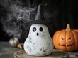 © Sevdaya - A speckled white ghost figurine wearing a sparkly black witch hat stands next to a small orange pumpkin against a dark, smoky backdrop.