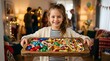 © Olinka N - A young girl with a big smile holds a wooden tray filled with various candies. Friends and family chat in the background at a festive event in a warm living room