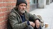 © Nazlykhan - Homeless man sitting on city sidewalk against brick wall. Mature beggar in dirty clothes asking for help. Social issue of poverty and unemployment. Despair and economic hardship.