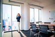 © gzorgz - Full length of a confident businesswoman in a modern glass-walled office with cityscape