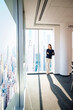© gzorgz - Full length of a confident businesswoman in a modern glass-walled office with cityscape