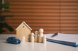© Custard Pixel - Family insurance planning with wooden house car and figurines beside policy documents representing financial protection asset coverage security and future stability.
