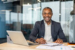 © Liubomir - Smiling african businessman writing on documents at his desk, having a laptop and office supplies, portraying success, professionalism, and confidence in a corporate environment