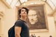 © EdvvinStudios - Young person stands in museum looking at large portrait in background during daytime visit