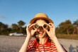 © SHOTPRIME STUDIO - Smiling woman in a straw hat and striped shirt peers through binoculars on a sunny beach, capturing a playful outdoor lifestyle moment and a sense of adventure.
