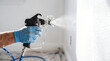 © solom - Professional painter spraying white coating on interior wall using airless spray gun during home renovation and painting project