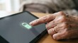 © SimpleDesignStudio - Elderly woman touching a tablet screen displaying a green battery charging icon representing technology accessibility