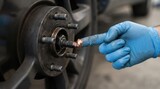 Mechanic applying copper grease to car wheel hub bolts during brake maintenance in garage