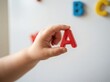 © SimpleDesignStudio - Toddler hand holding a red letter A magnet for early childhood education and alphabet learning