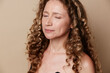 © SHOTPRIME STUDIO - Authentic middle-aged woman with natural skin and curly hair posing on a brown background. Close-up portrait emphasizing genuine beauty and wellness.