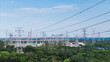 © tai - An outdoor high voltage power substation with multiple transmission towers and power lines, surrounded by green vegetation under a clear sky.