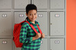 © Pixel-Shot - Teenage African-American schoolboy with backpack near locker on orange background