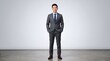 © Wei - Full body portrait of confident Asian businessman standing in grey suit against white studio background, hands in pockets, smiling at camera, corporate professional image.