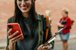 © La Famiglia - Young student smiling and using smartphone on campus