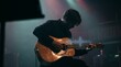 © mtsrprn - Silhouette of a young musician playing an acoustic guitar on a dimly lit stage during a live concert performance