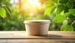© Hamdan - Blank eco-friendly paper food container mockup sitting on a wooden table outdoors with green foliage.