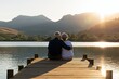 © oksa_studio - Senior couple sitting on a wooden pier by a calm lake during a romantic sunset