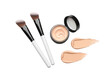 © Ferdous - Two angled makeup brushes with white handles, a small open jar of beige liquid foundation, and two smooth cream texture swatches isolated on a black background