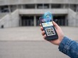 © Solonery Tech - Hand holding smartphone with digital concert ticket and holographic AR seat locator pin in front of blurred stadium entrance