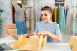 © Kawee - Caucasian woman packing clothes into cardboard boxes for online orders in store.