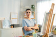 © Kawee - Portrait of female artist painting artwork on canvas frame at home studio.