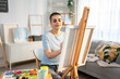© Kawee - Caucasian female artist painting artwork on canvas frame at home studio.