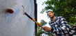 © ronstik - House painter applying protective coating on house exterior wall with roller. Facade protection against algae, moss and fungal