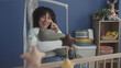 © Krakenimages.com - Woman cradles baby and talks on phone by crib mobile in studio, smiling and soothing with hand on swaddled head; tenderness bonding.