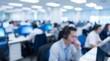© CuteBee - Customer service agent wearing headset working on computer in bright open plan office with blurred background of busy call center employees during daily operations and communication tasks