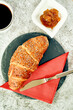 © Joachim - Buttery croissant on ceramic plate with apricot jam and knife, set at cafe table. Red napkin.