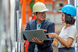 © atitaph - Asian factory manager showing steel coil details on laptop to female engineer in warehouse