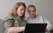 © atikinka2 - Mid adult couple sitting on a sofa at home looking at a tablet with thoughtful expressions while discussing information, making a decision, planning finances, reviewing documents, solving a problem.