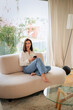 © gzorgz - Attractive brown haired woman texting on her mobile phone while sitting on a modern couch