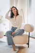 © gzorgz - Full length of a cheerful smiling woman sitting in an armchair in her modern home