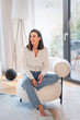 © gzorgz - Full length of a cheerful smiling woman sitting in an armchair in her modern home