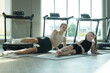 © ultramansk - Sporty young woman and her girl in black leggings raise straight legs high lying on their sides at their morning exercise session in the gym, authentic everyday scene