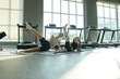 © ultramansk - Young mother and her little daughter in sportswear lift single legs skyward in side lying position during a family workout in a modern sunlit fitness studio with copy space