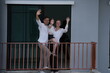 © ultramansk - Caucasian family of three embracing laugh and wave from the new balcony railing standing on the terrace of a newly built suburban home. Healthy active lifestyle of a modern family