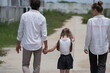 © ultramansk - Young couple with their laughing daughter stroll along the unpaved street of the new development holding hands on a walk through a new suburban housing development, authentic everyday scene