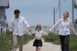 © ultramansk - Happy young family with little daughter walk hand in hand down the dirt road toward their future home outdoors on the street of a newly built residential neighborhood, candid real moment